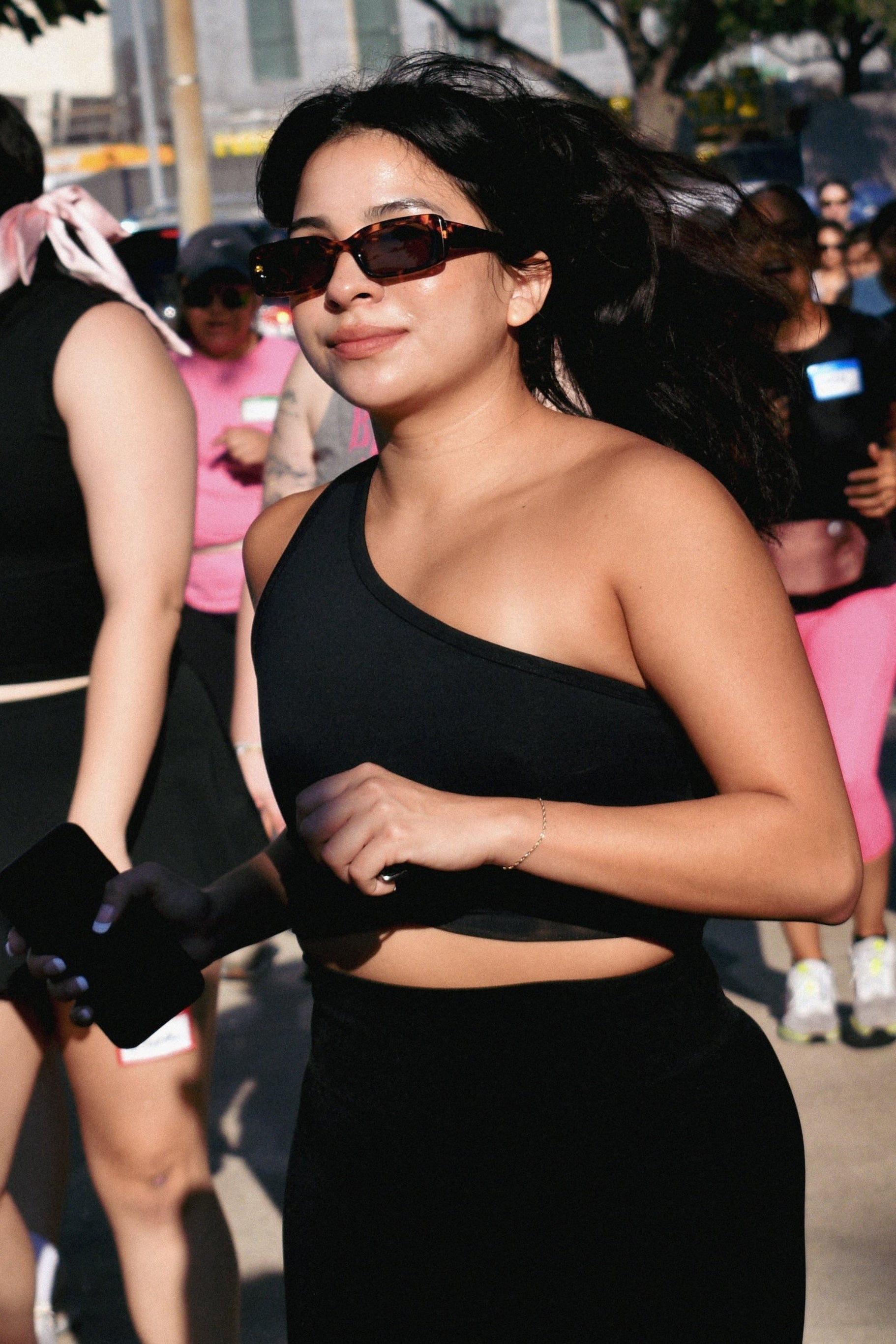 Woman in black athletic wear and sunglasses walking outdoors with blurred background